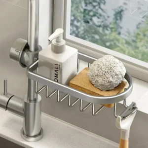 Sink drain rack hooked over a kitchen faucet holding a sponge, soap bar, and cleaning brush in a slatted aluminum basket